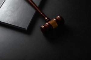 Na ciemnym tle widoczny jest drewniany młotek sędziowski leżący obok zamkniętej książki