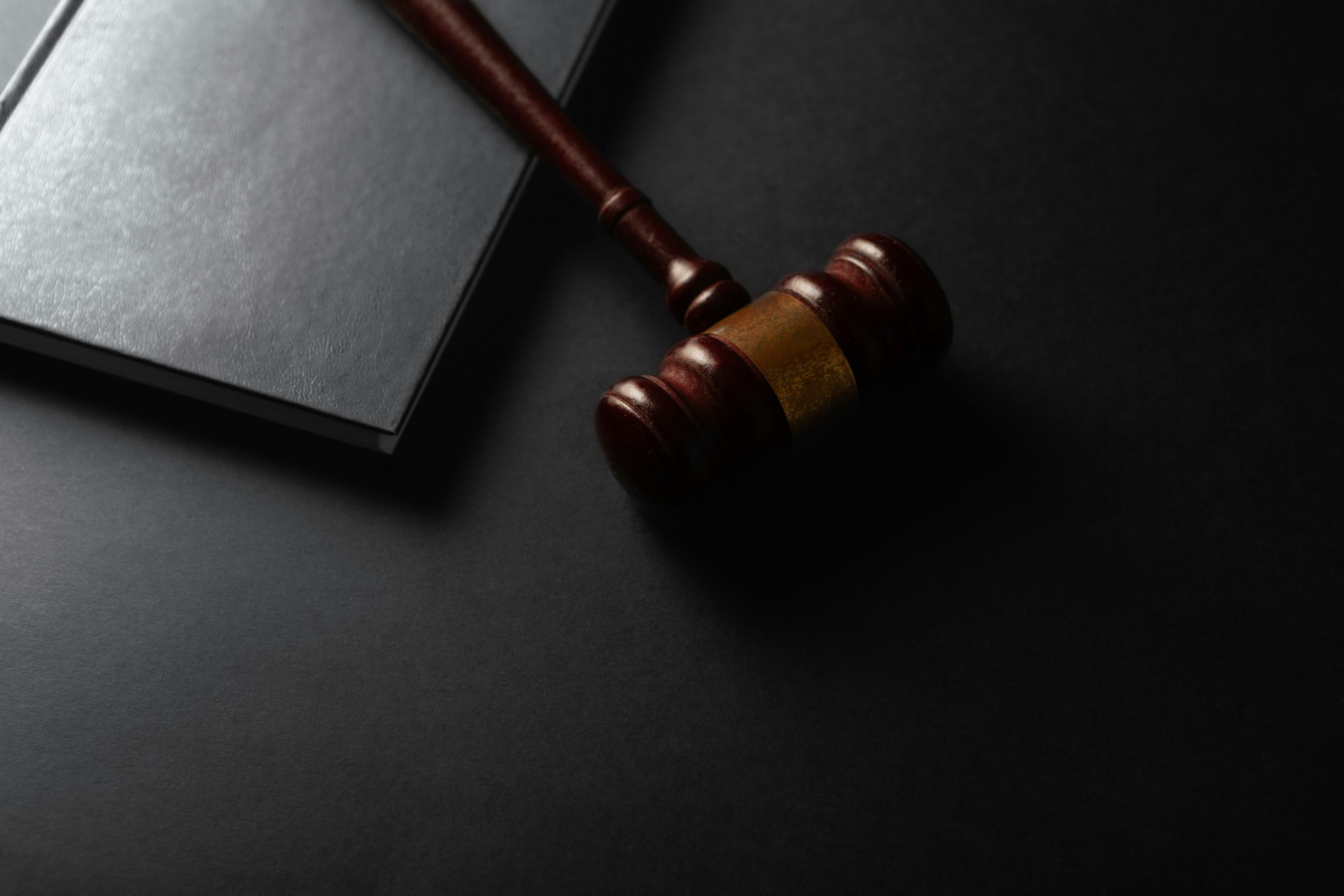 Na ciemnym tle widoczny jest drewniany młotek sędziowski leżący obok zamkniętej książki