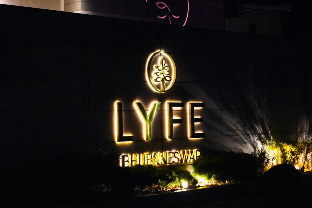Fotografia przedstawia nocną scenę z podświetlanym szyldem „LYFE BHUBANESWAR” umieszczonym na ścianie budynku
