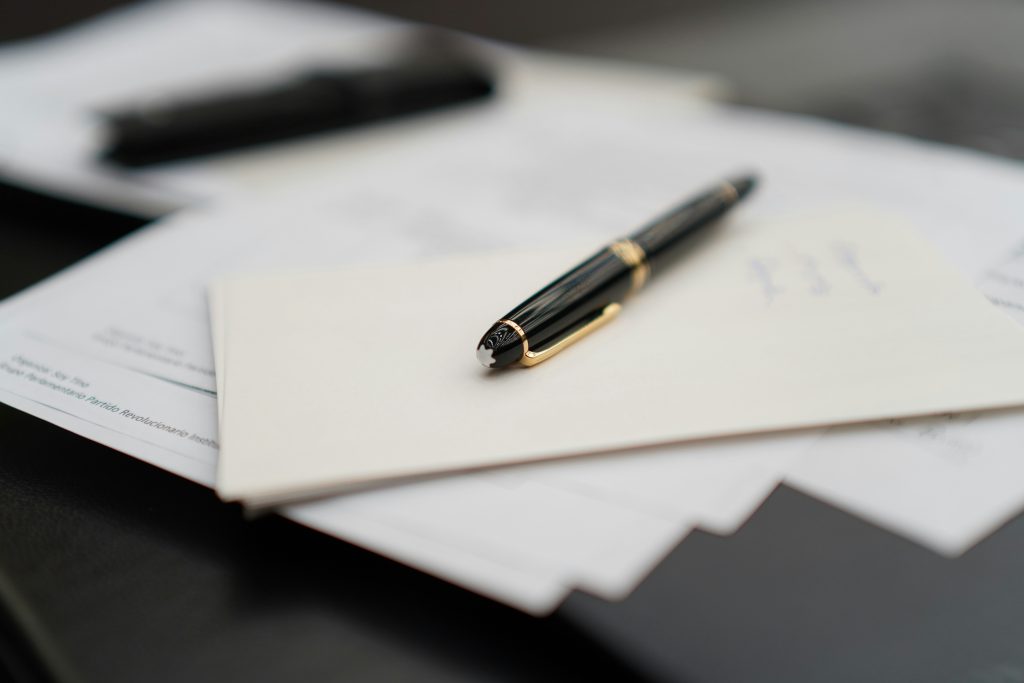 Na zdjęciu przedstawiono eleganckie pióro spoczywające na kopercie, która leży na dokumentach