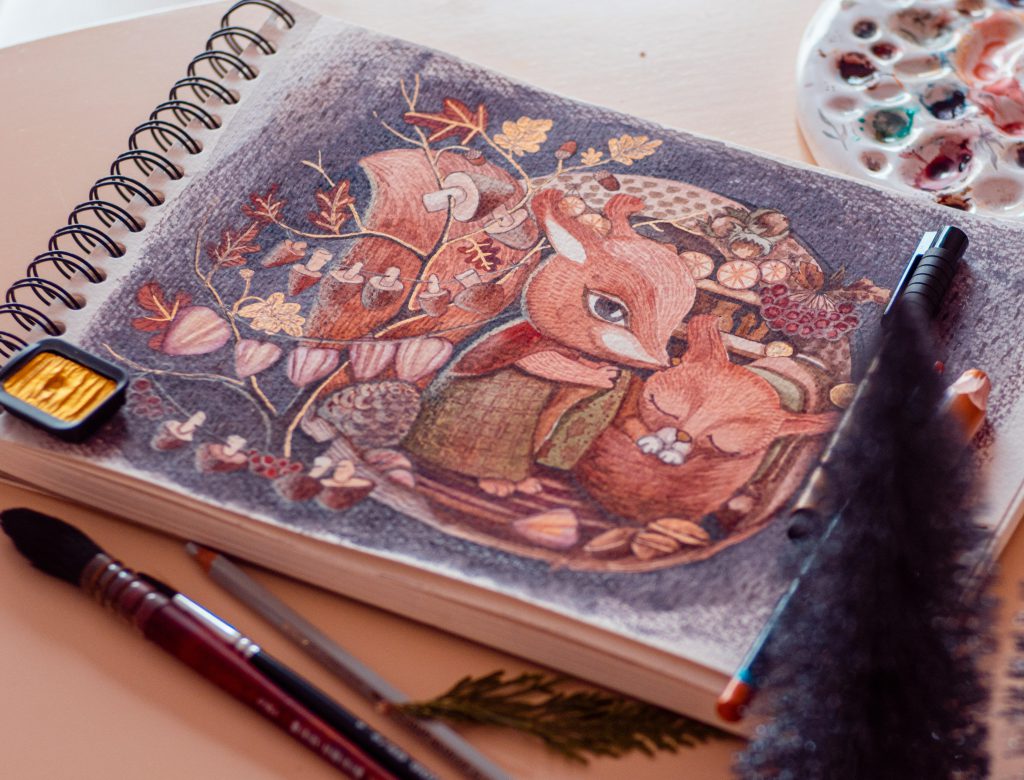 Na zdjęciu widoczny jest szkicownik otwarty na ilustracji przedstawiającej dwa lisy w leśnym otoczeniu