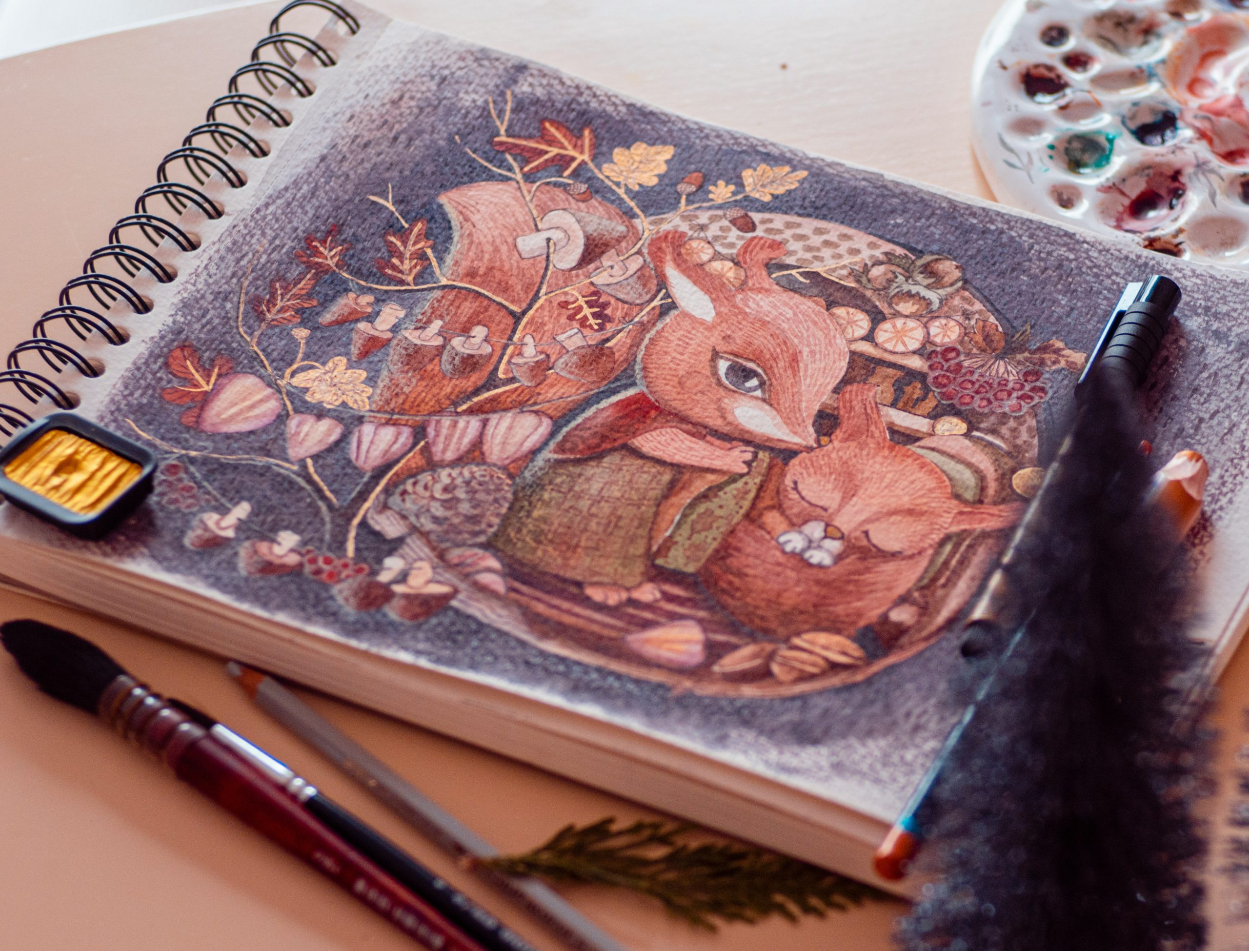 Na zdjęciu widoczny jest szkicownik otwarty na ilustracji przedstawiającej dwa lisy w leśnym otoczeniu