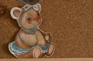 Na zdjęciu widać ilustrację przedstawiającą uroczego, ręcznie malowanego misia przypiętego do korkowej tablicy