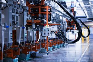 Na zdjęciu przedstawiona jest zaawansowana linia przemysłowa z pomarańczowymi modułami maszyn i licznymi przewodami zwisającymi z konstrukcji