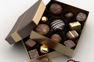 Eleganckie bombonierki z logo w złotym pudełku, wypełnione różnorodnymi czekoladkami rzemieślniczymi i pralinami z posypką.