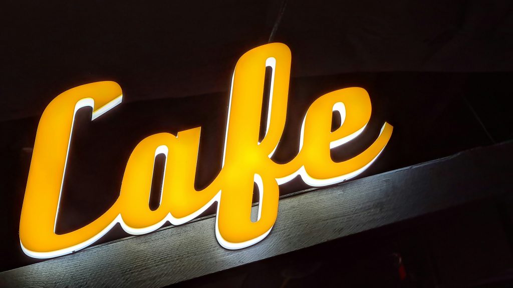 Na zdjęciu znajduje się podświetlany napis „Cafe” w intensywnym, ciepłym żółtym kolorze